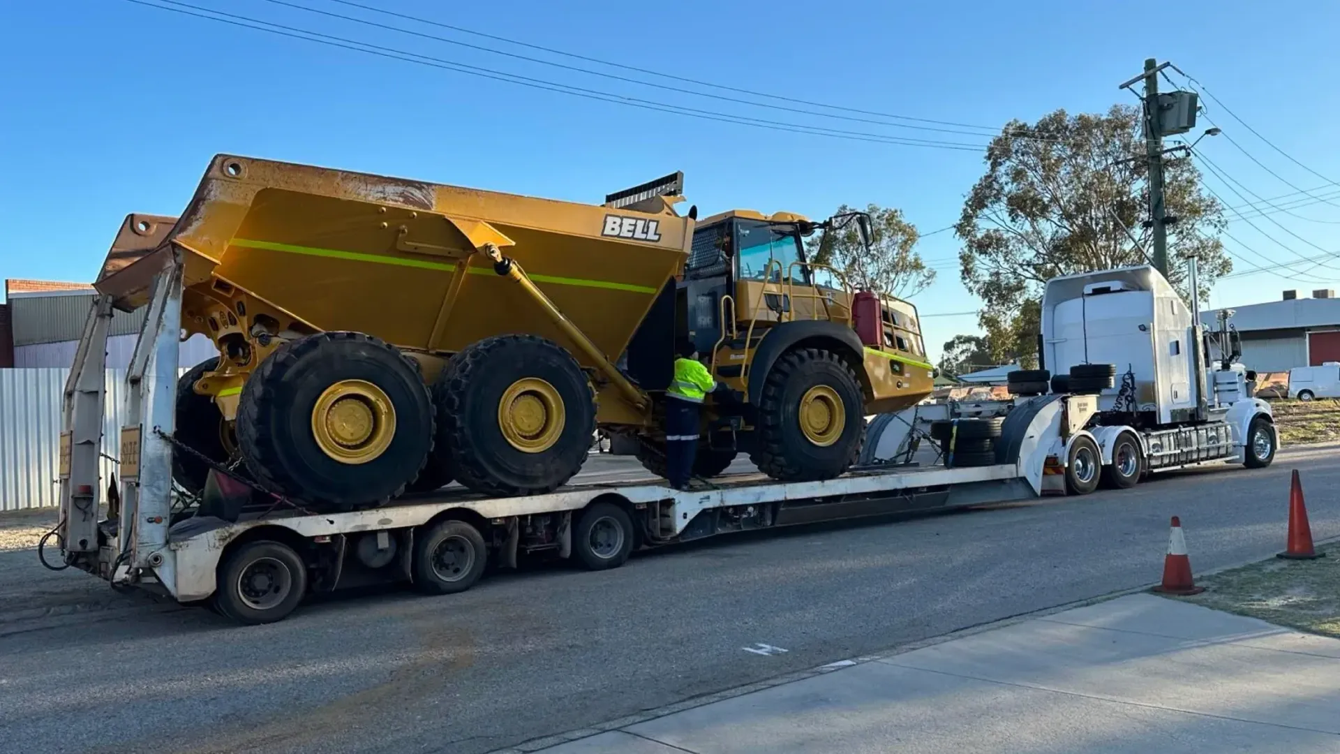 Yellow Dump Truck on a Flatbed Trailer Being Transported Down a Road by a Semi-truck — Supertilt Brisbane In Brendale, QLD