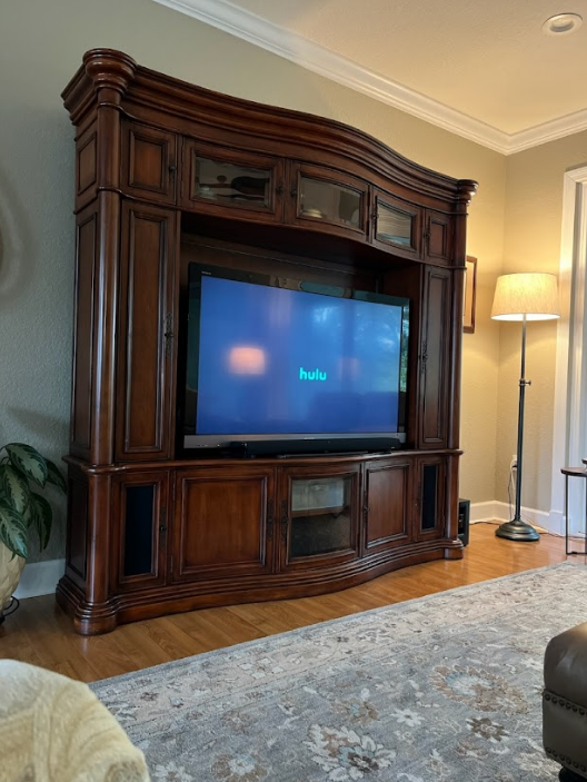 Large wooden entertainment center with TV, soundbar, and storage cabinets. A floor lamp is in the background.