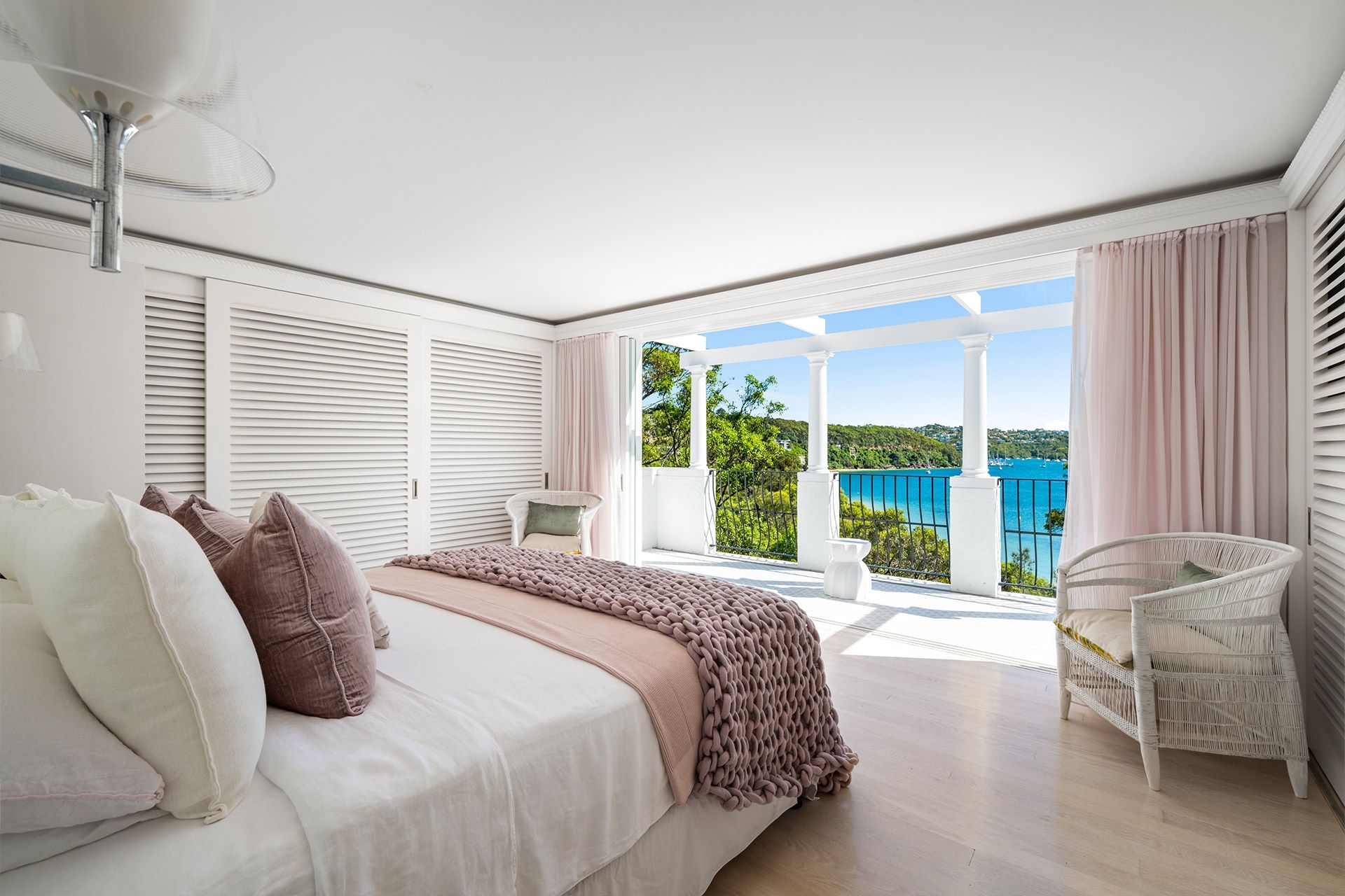 A bedroom with a large bed and a chair with a view of the ocean. Mosman.