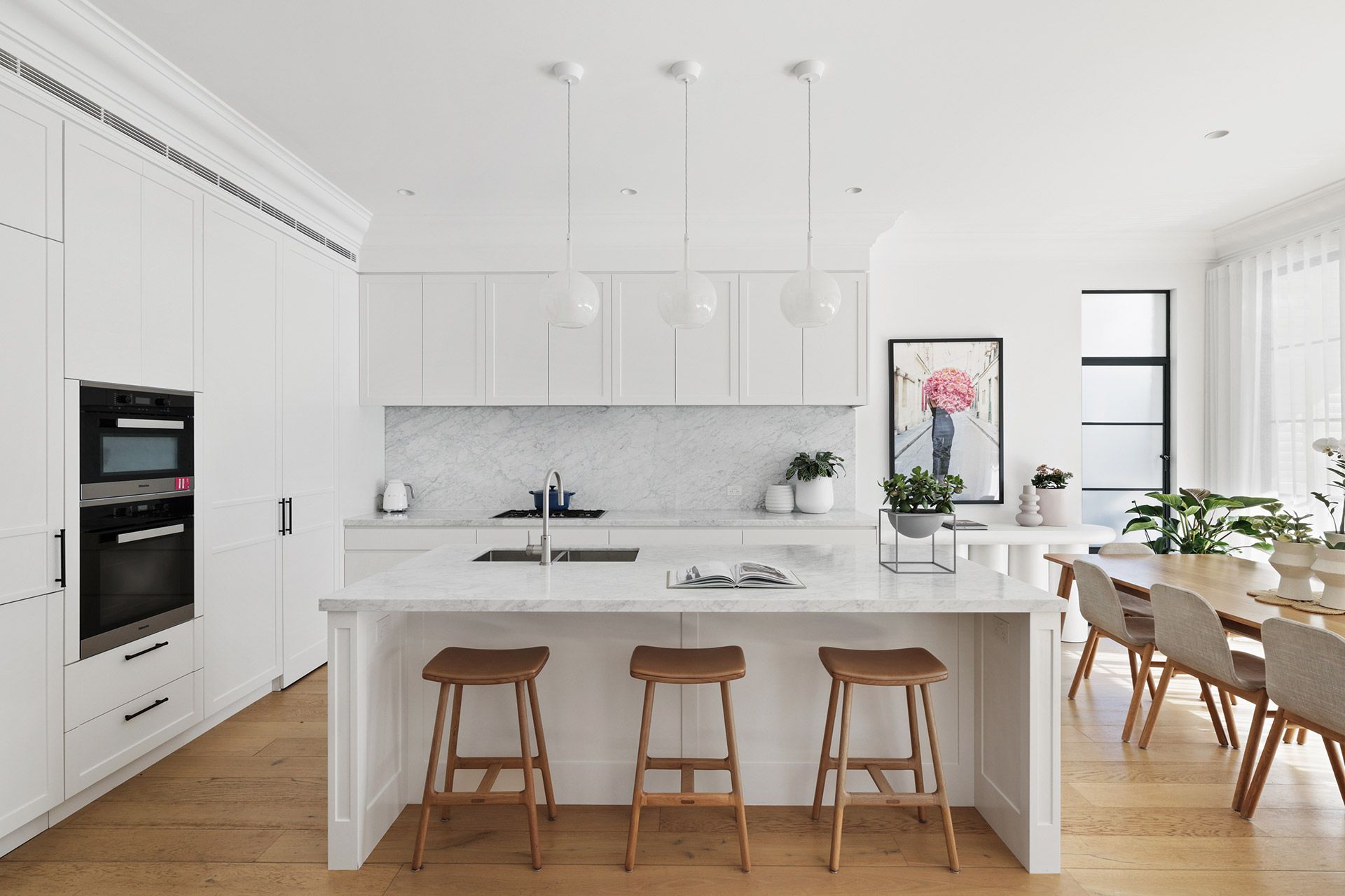 A kitchen with white cabinets , wooden floors , stools and a large island. Mosman