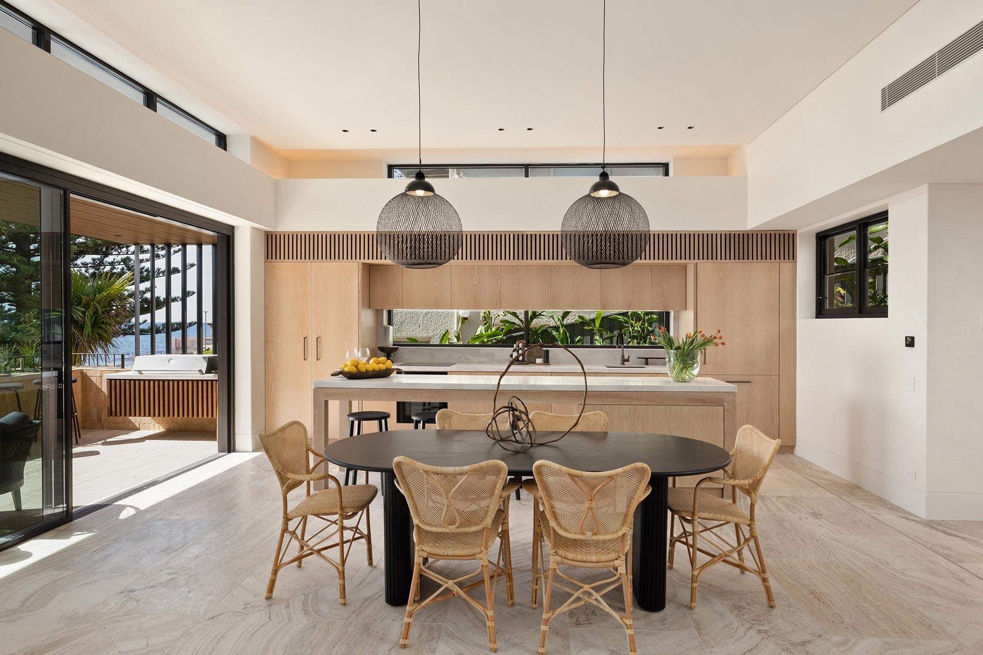 A dining room with a table and chairs and a kitchen in the background.