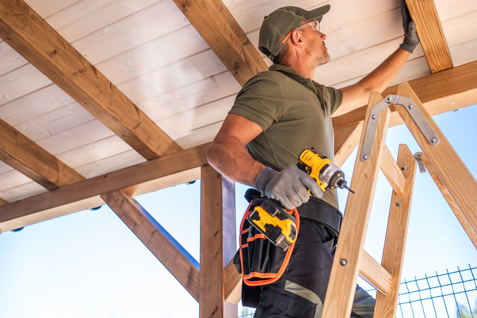 A man is standing on a ladder working on a wooden structure.