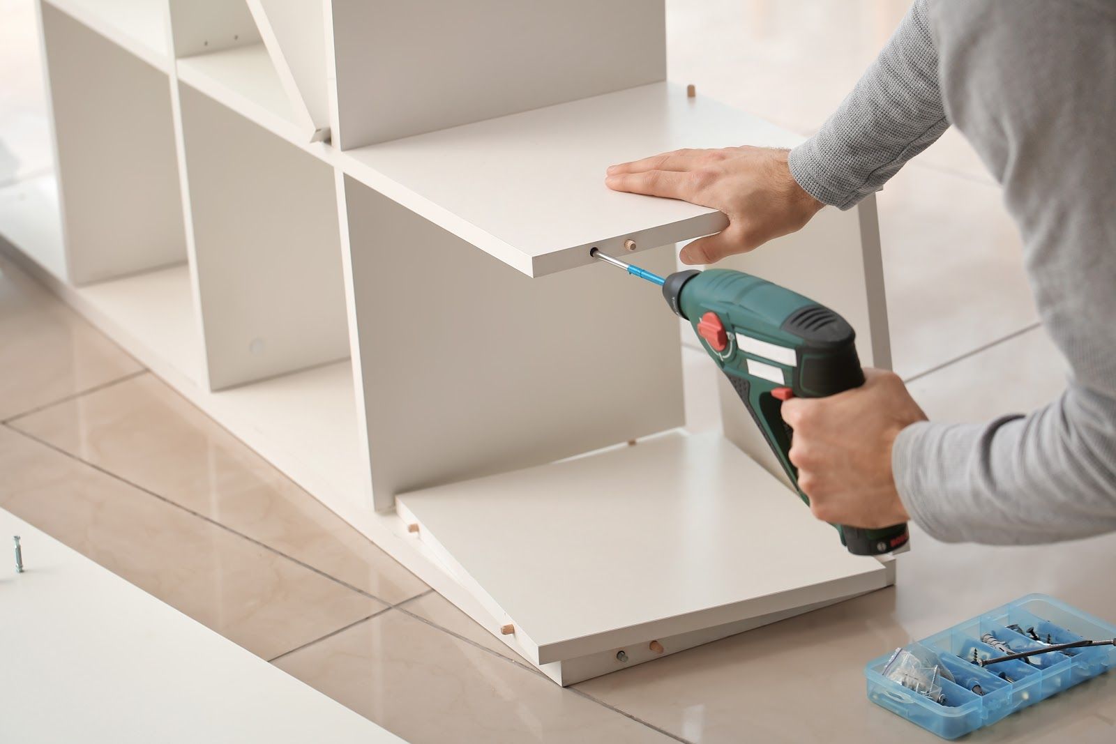 Person assembling white cube shelf with a drill.