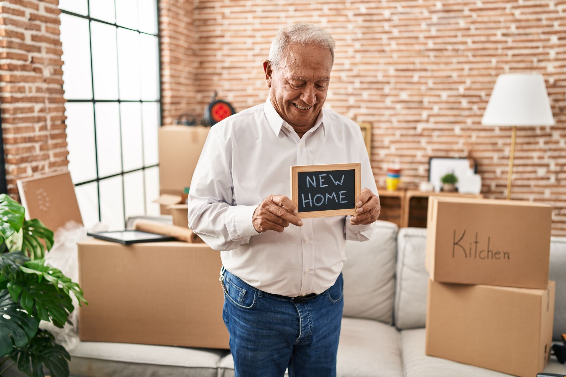 An elderly man is holding a sign that says  ''new home '' in a living room.