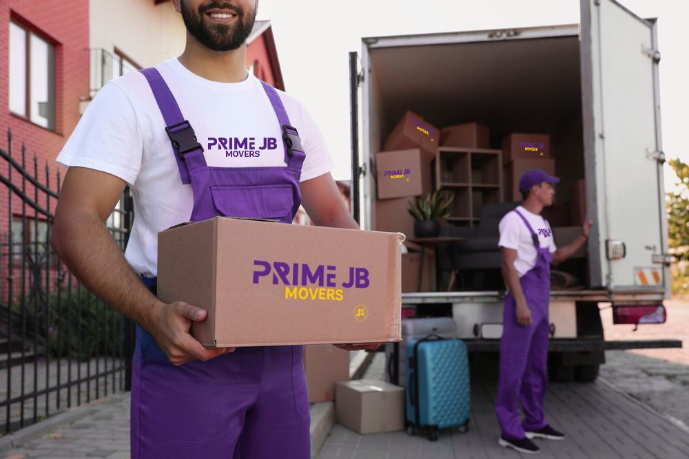 Moving company employees loading a truck. One holds a box; others are in the truck. Purple and white uniforms.