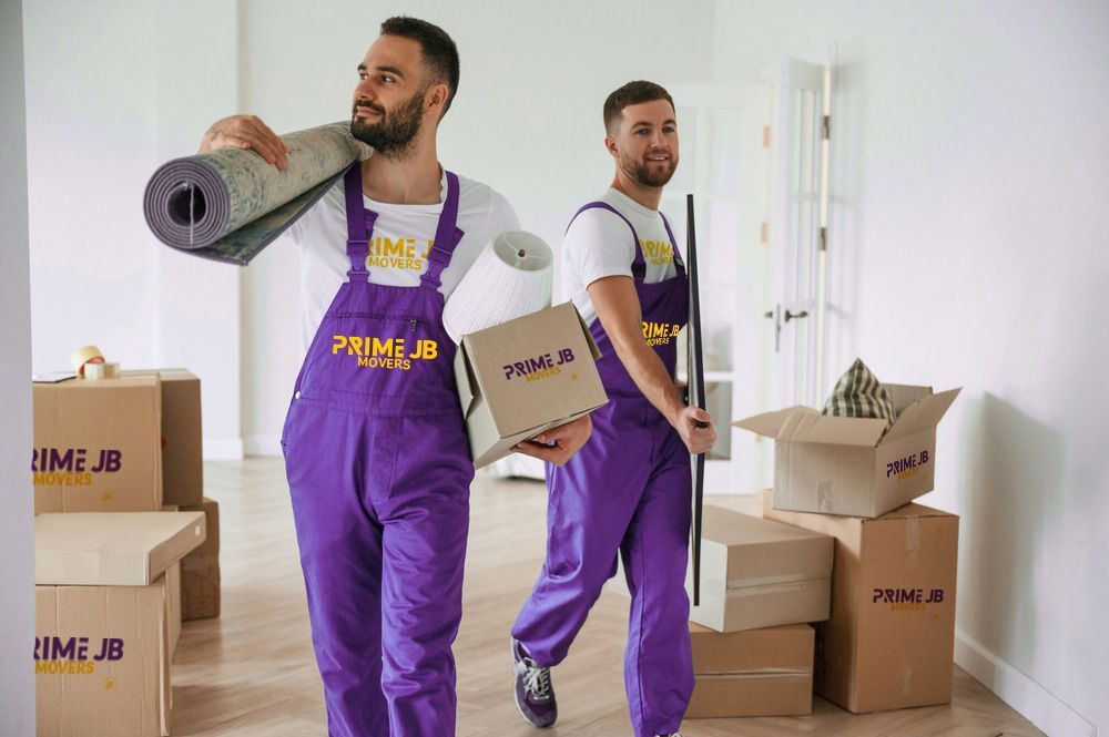 Two men in purple overalls are carrying boxes and a rug.