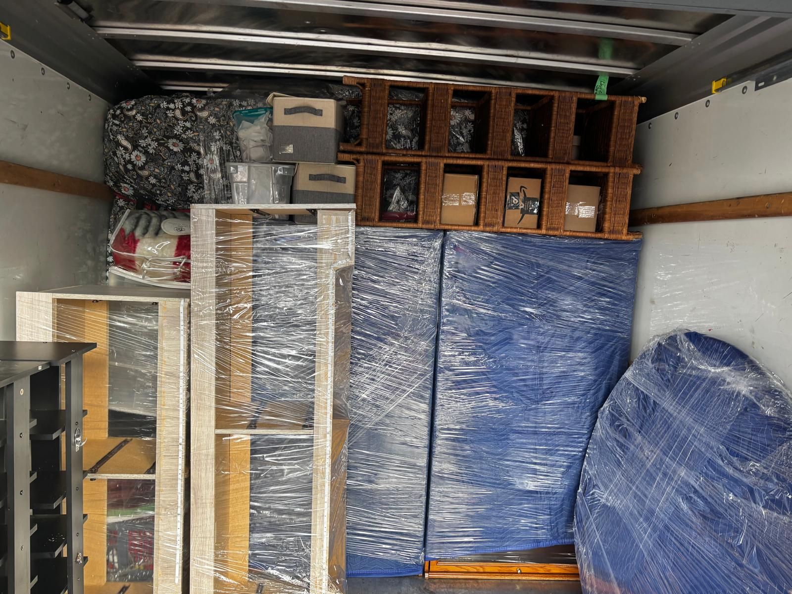 Interior of a moving truck packed with furniture, wrapped in plastic and blue pads, and boxes.