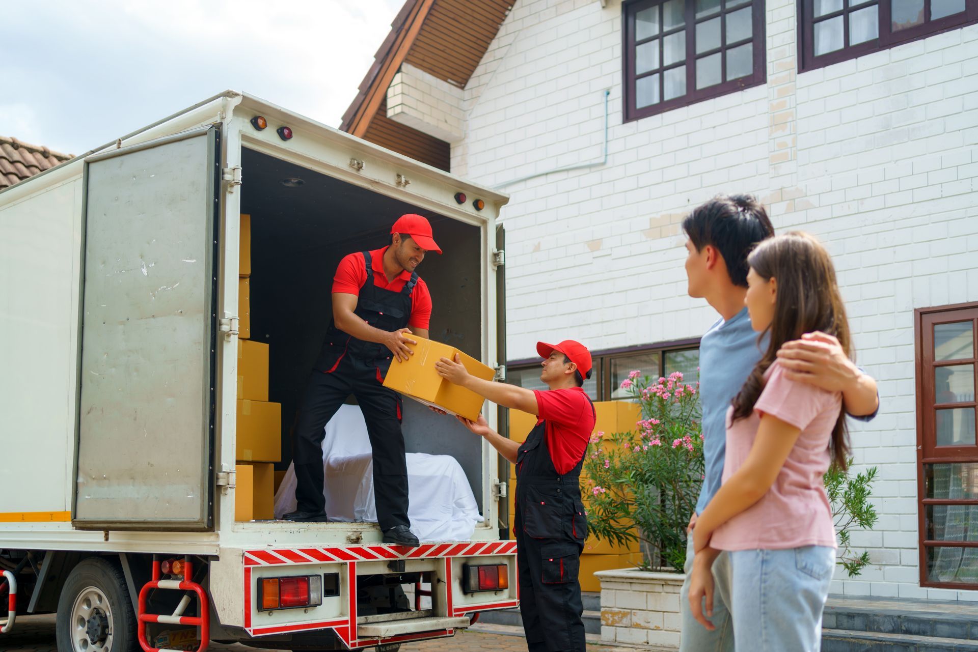 A man is giving a box to a woman in front of a moving truck.
