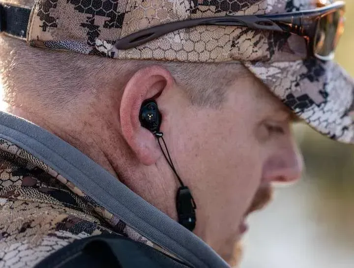 A man wearing a hat and sunglasses is wearing earbuds.