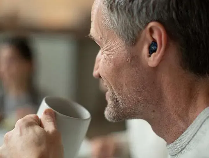 A man wearing hearing aids is drinking a cup of coffee.