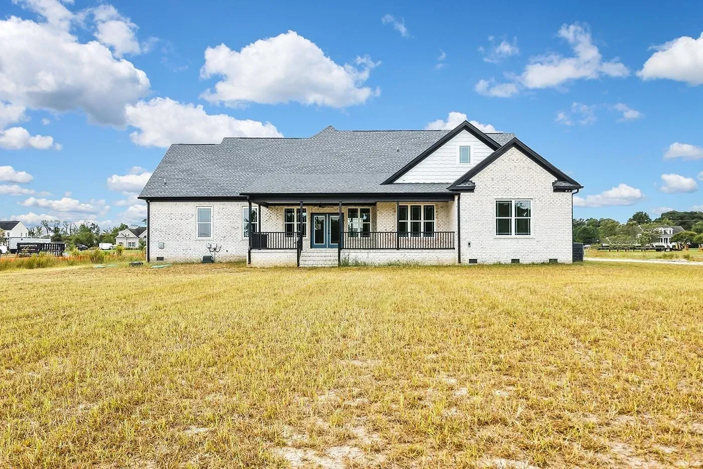 A single-story brick house with a dark roof and a porch on a grassy lot under a cloudy sky.