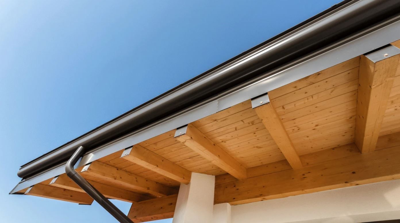 Wooden house eaves with metal gutter against a blue sky