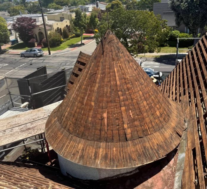 Aerial view of a rust-colored conical roof on a building beside a street and trees.