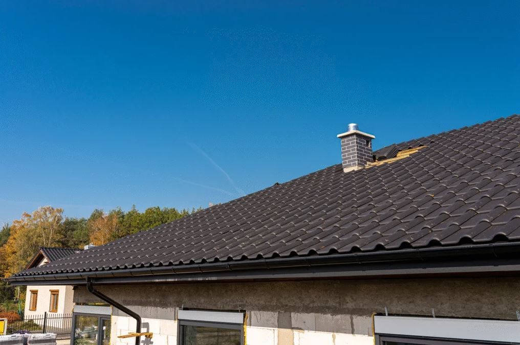 House roof with dark shingles and a chimney under a clear blue sky