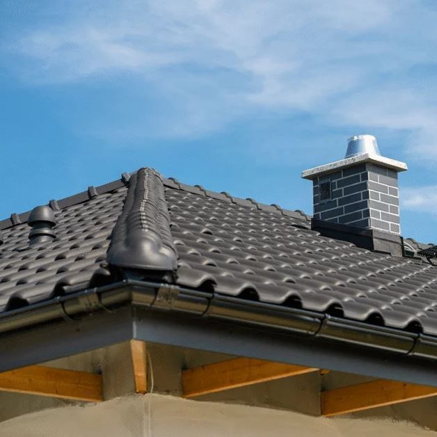 Dark gray tiled roof with a silver chimney under a blue sky