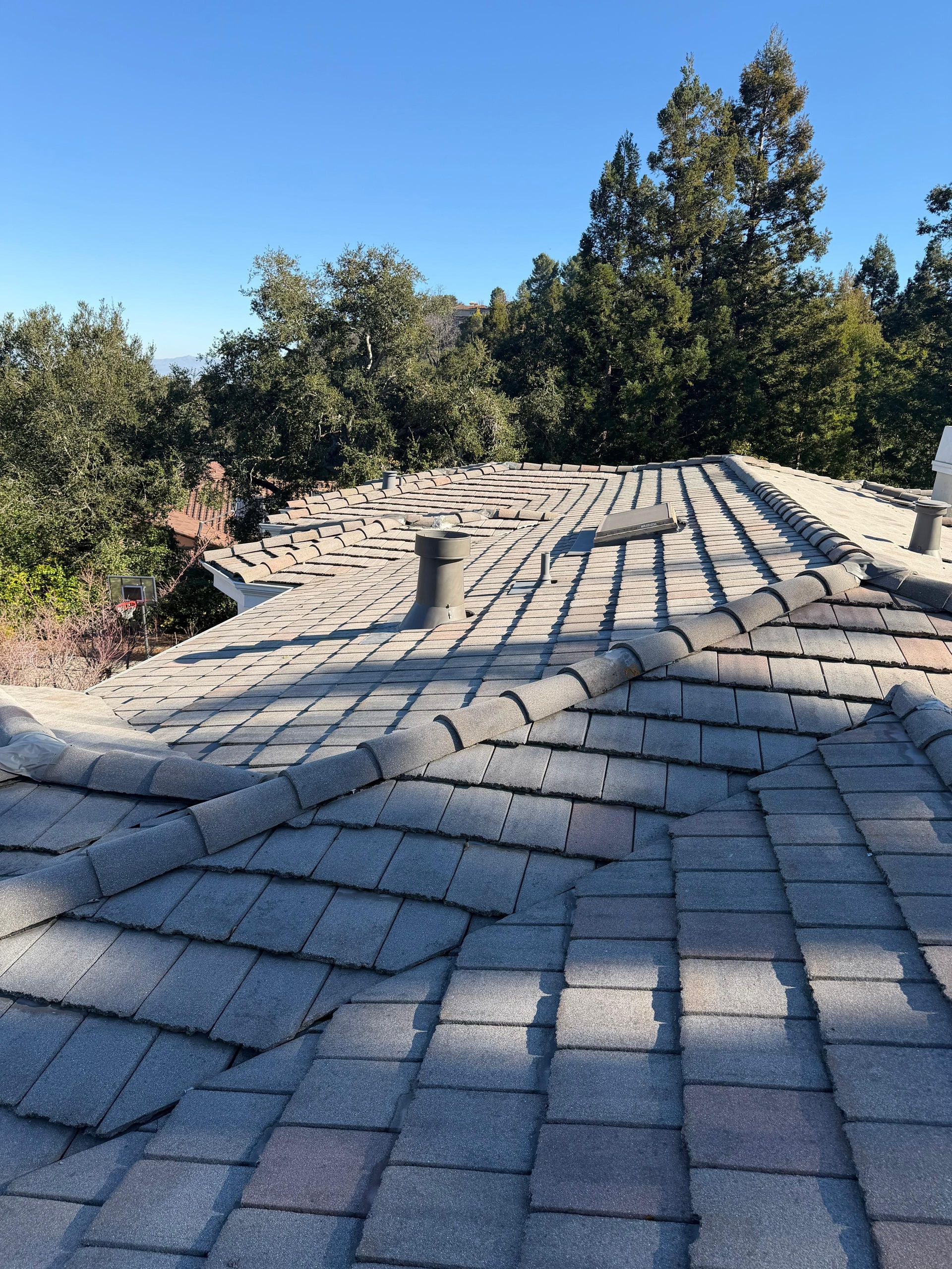 Collapsed shingle roof with warped gray tiles under trees in daylight
