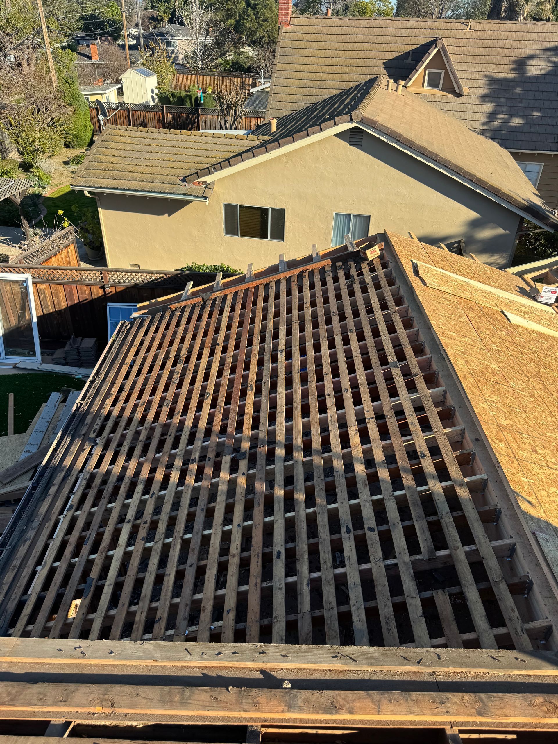 Roof under repair with exposed wooden slats and neighboring houses in the background.