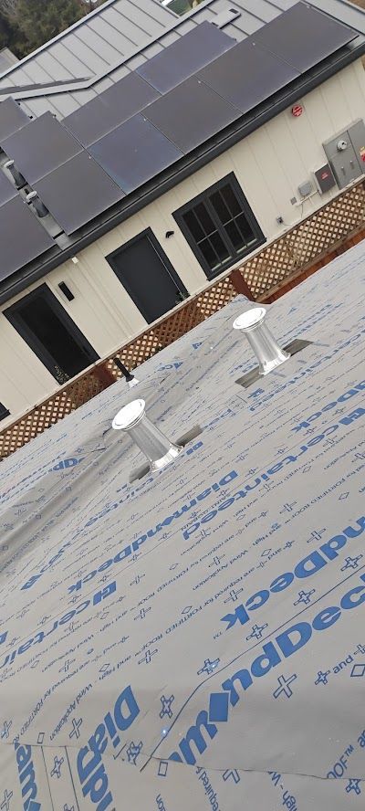 Roof under construction with white vents and solar panels on a building wall above.