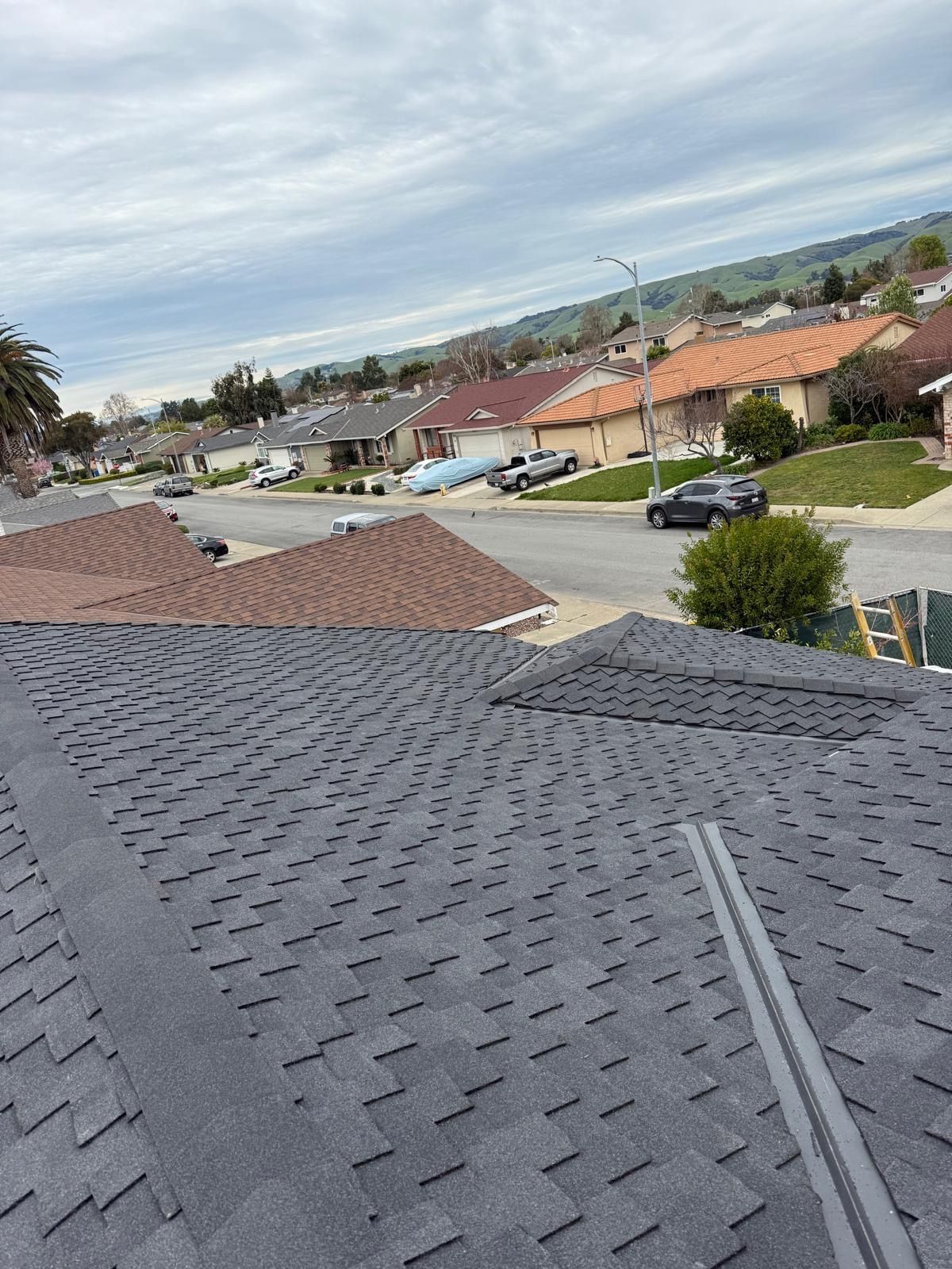 Rooftop view over a suburban neighborhood with tiled roofs, parked cars, and cloudy sky.