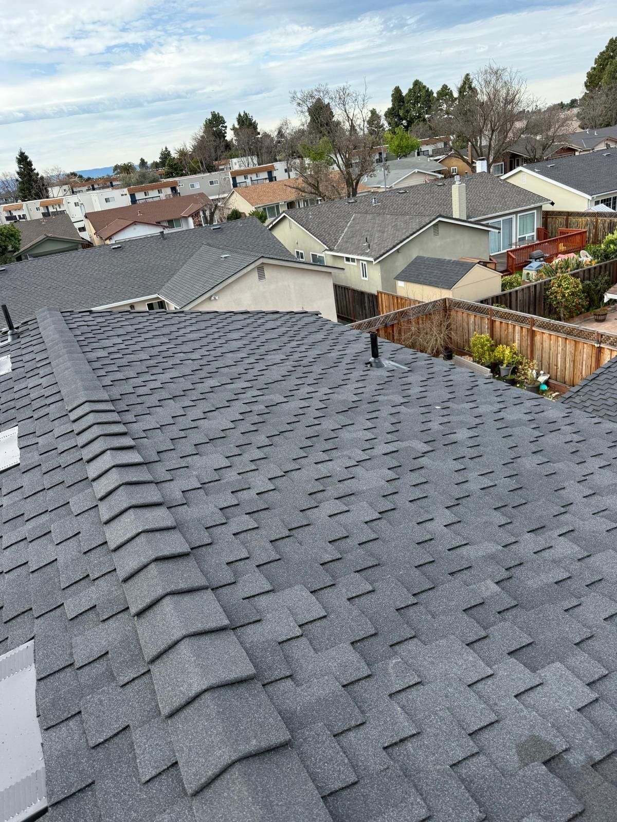 Gray shingled rooftop overlooking a suburban neighborhood under a cloudy sky