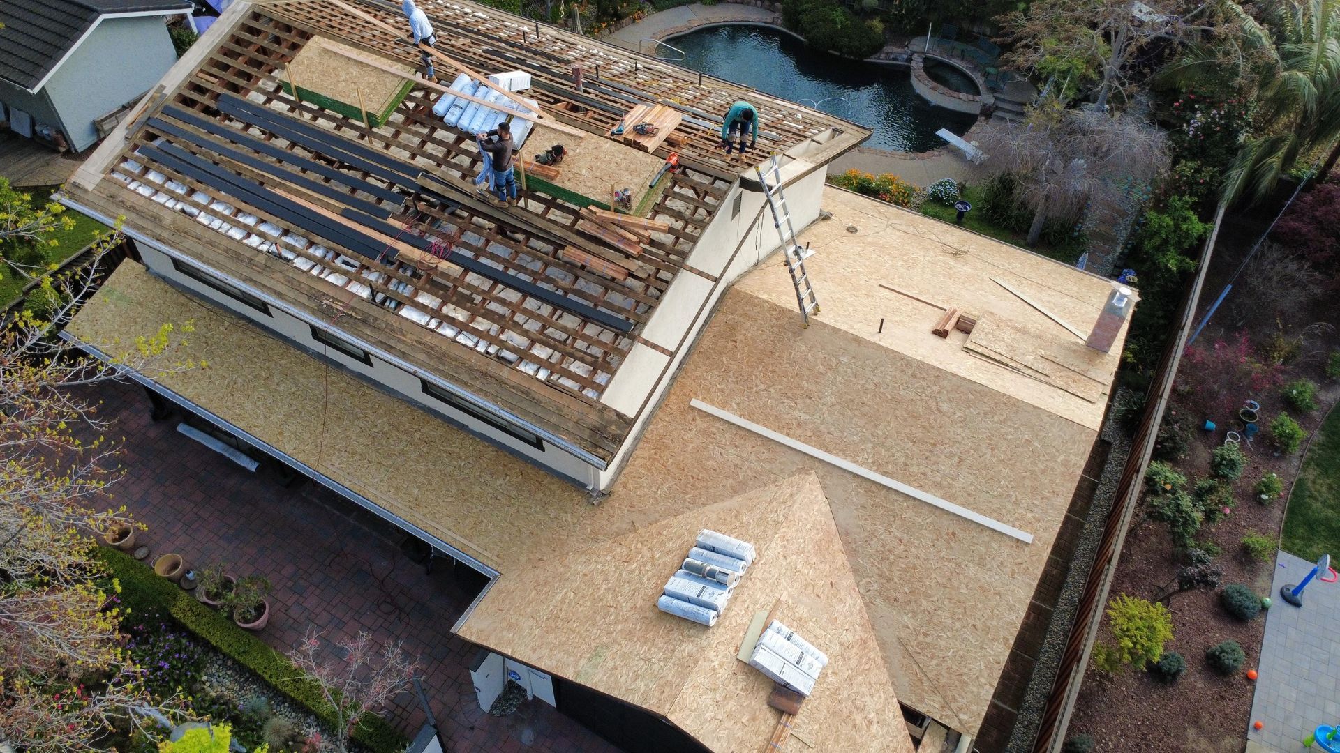 Aerial view of a house roof under construction with exposed beams and stacked roofing materials