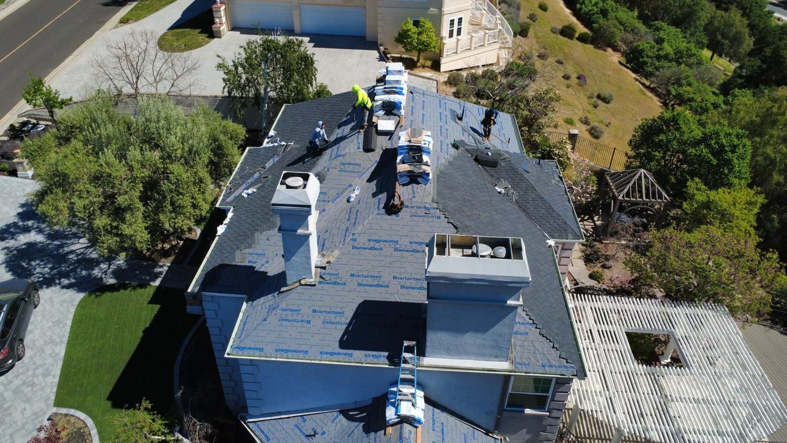Aerial view of a house with workers on the roof, surrounded by trees and a driveway.
