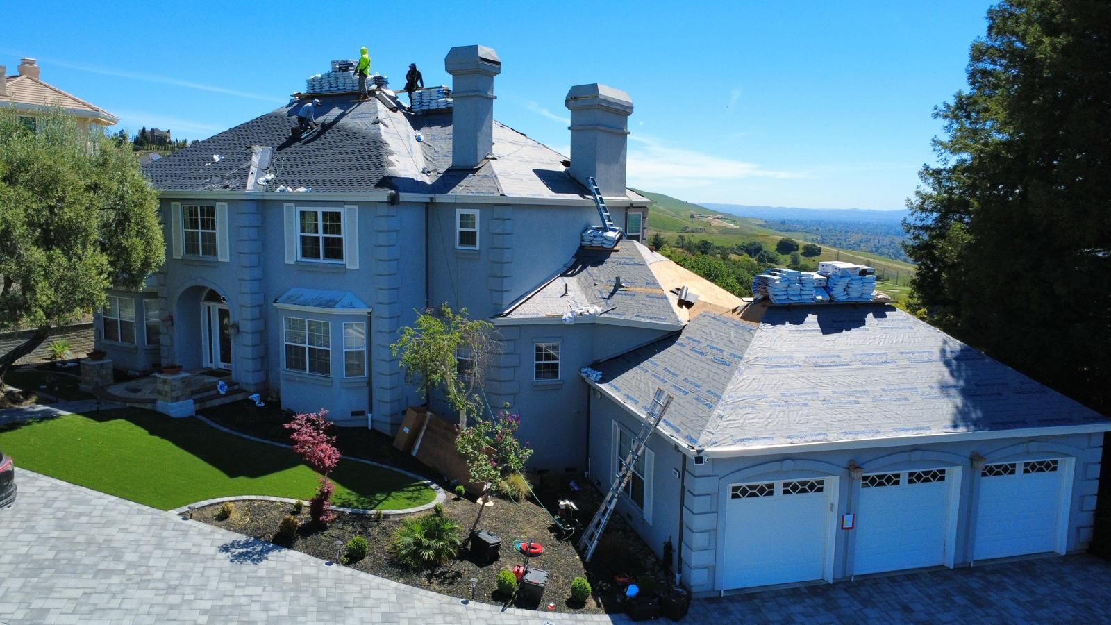 Large gray house with a white garage overlooking a landscaped yard and distant water under a blue sky