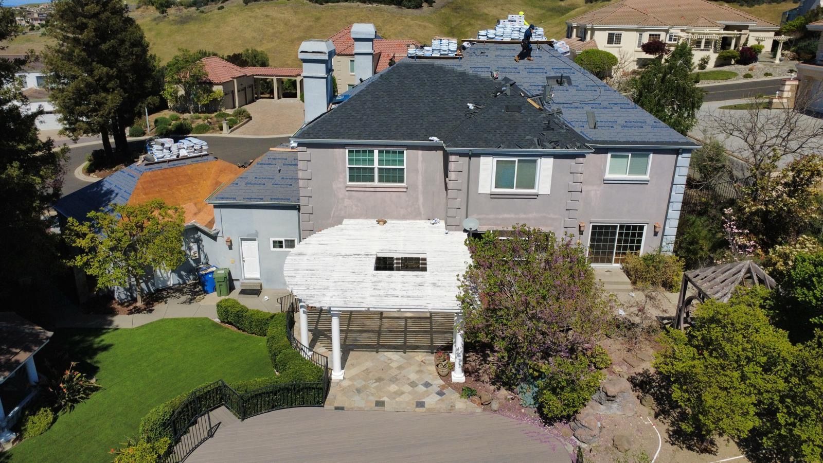 Aerial view of a two-story house with a driveway, front yard, and surrounding trees and neighboring homes.