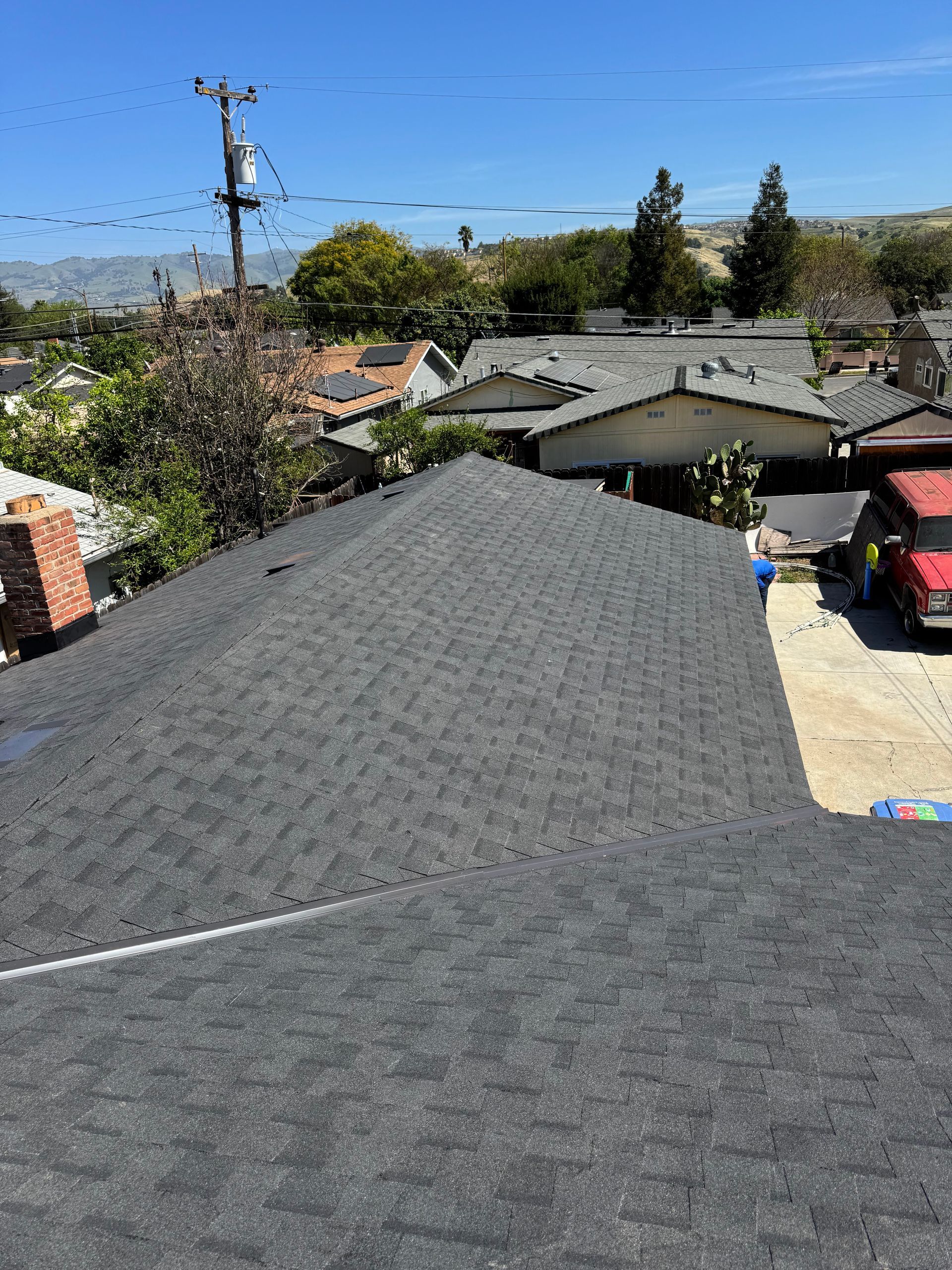 Rooftop view over suburban houses, trees, and power lines on a clear day.