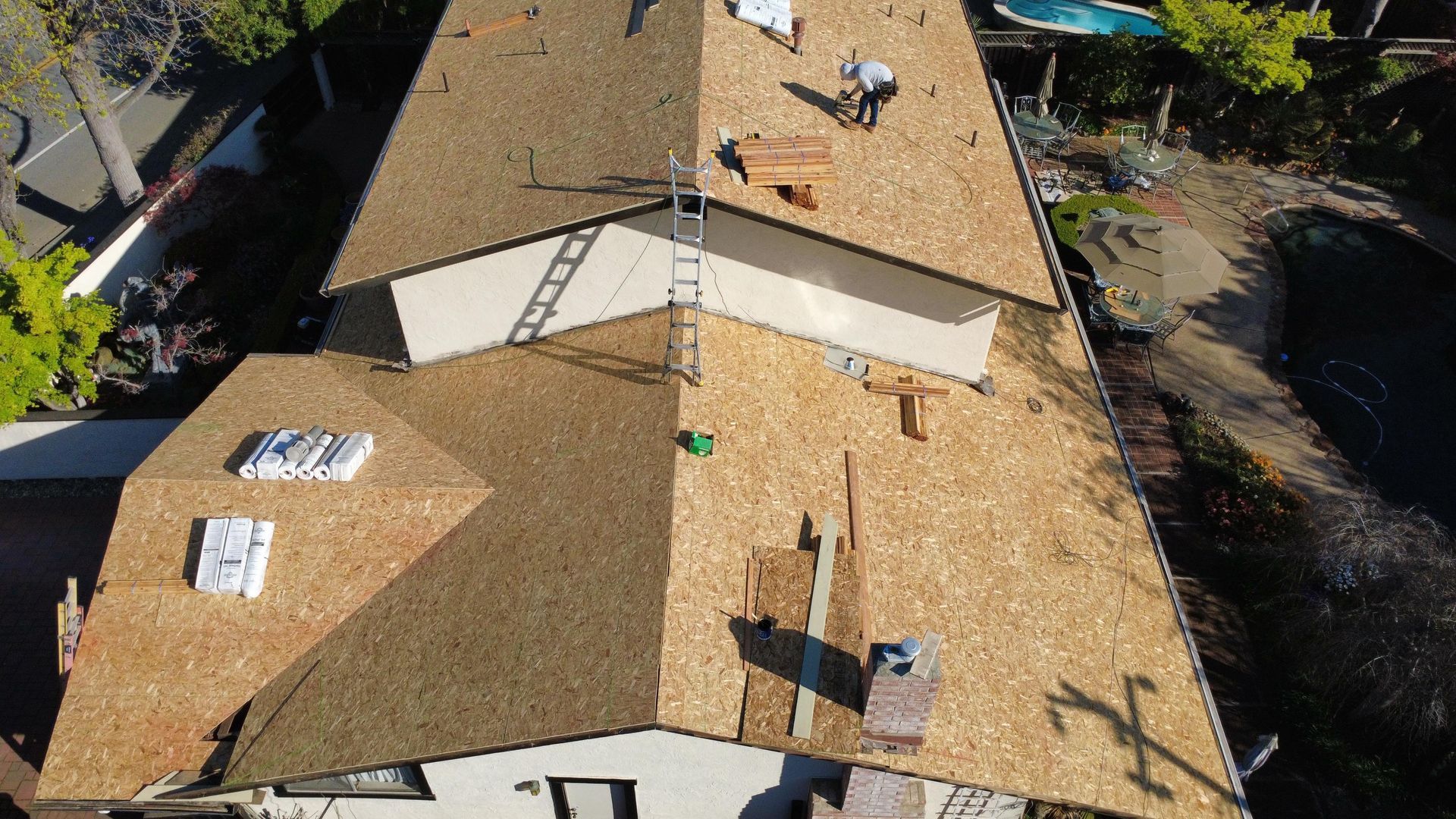 Aerial view of a shingled house roof with solar panels and rooftop vents in a residential neighborhood