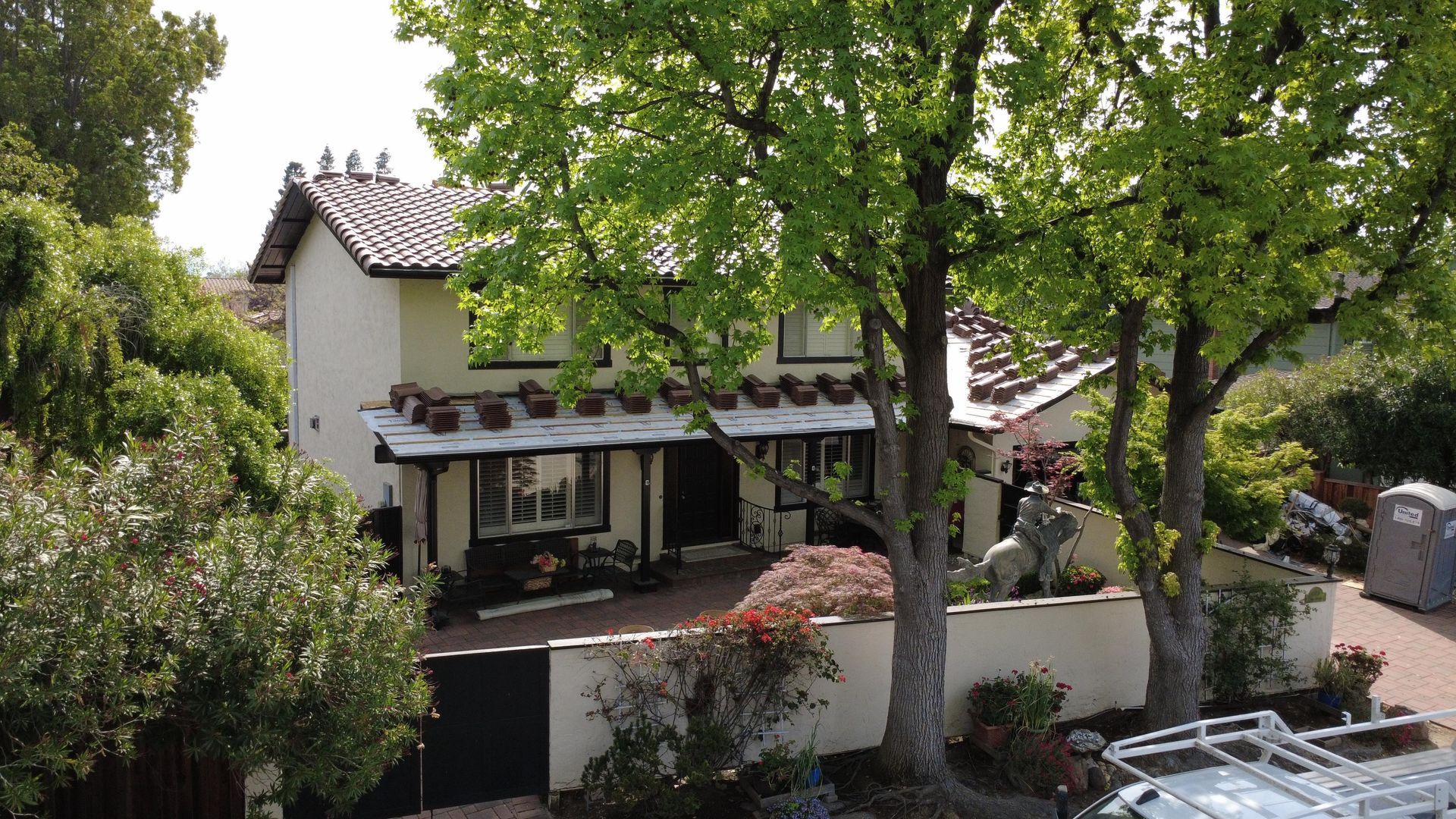 Courtyard house with red-tiled roof, white walls, and lush green trees in a sunny garden setting