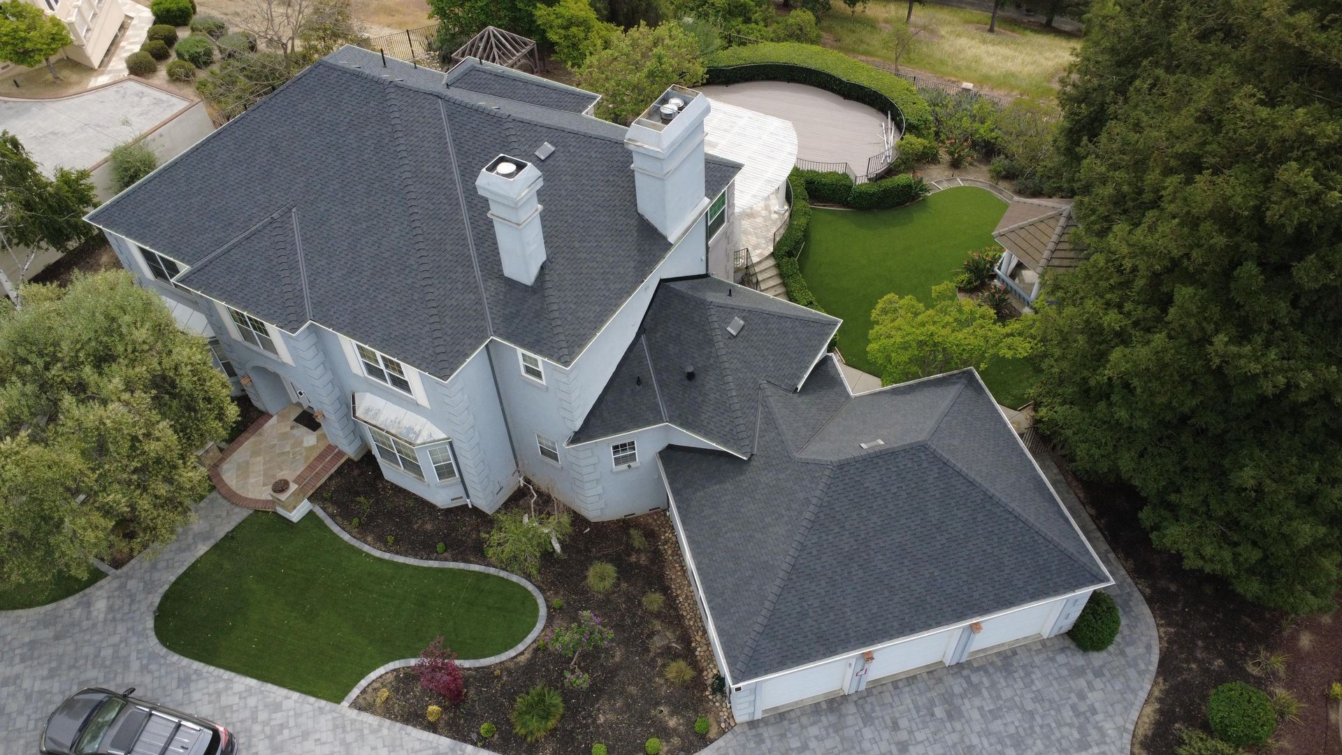 Aerial view of a gray-roofed two-story house with a garage and landscaped yard.