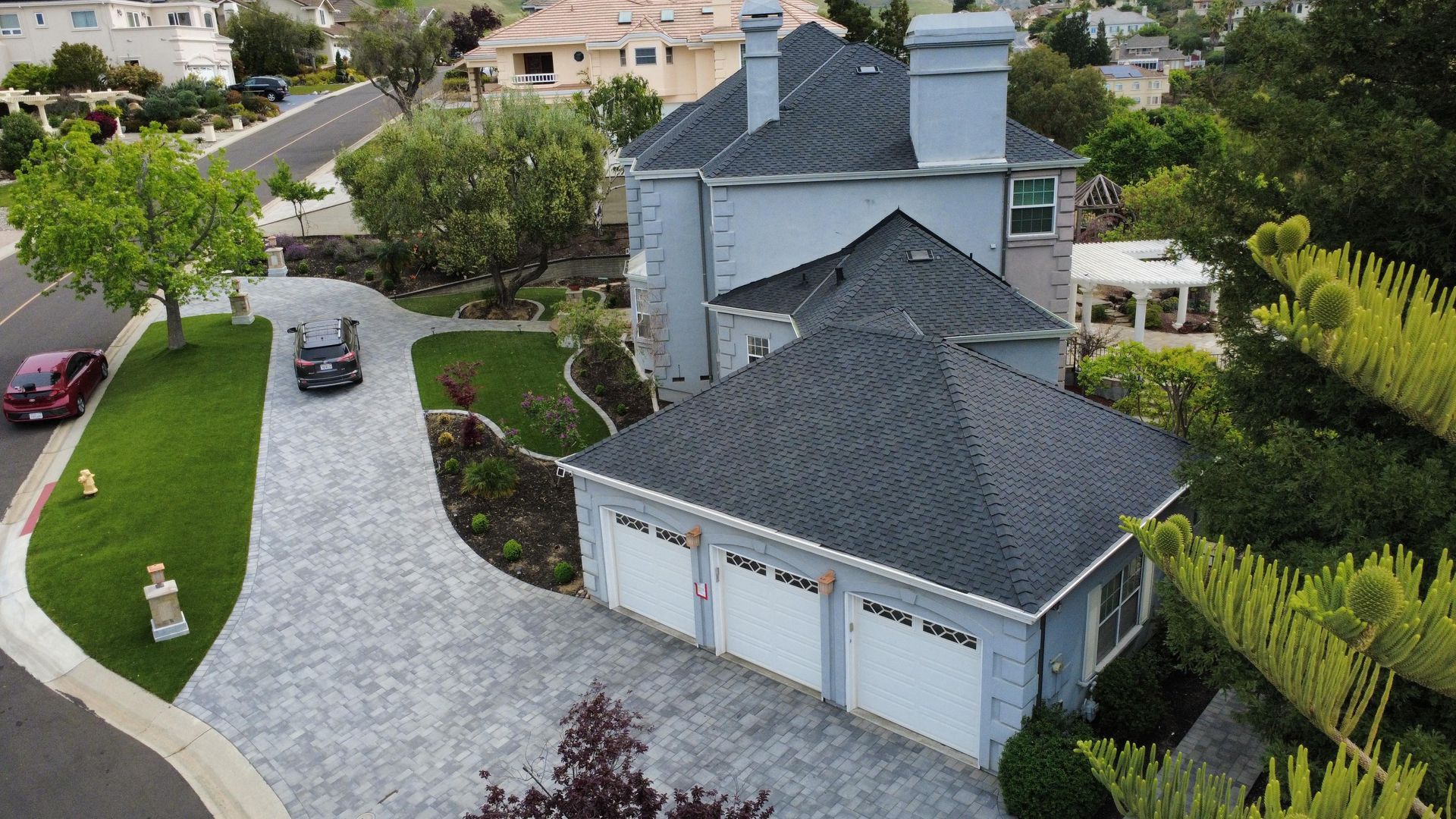Aerial view of a gray two-story house with a three-car garage and curved driveway in a suburban neighborhood