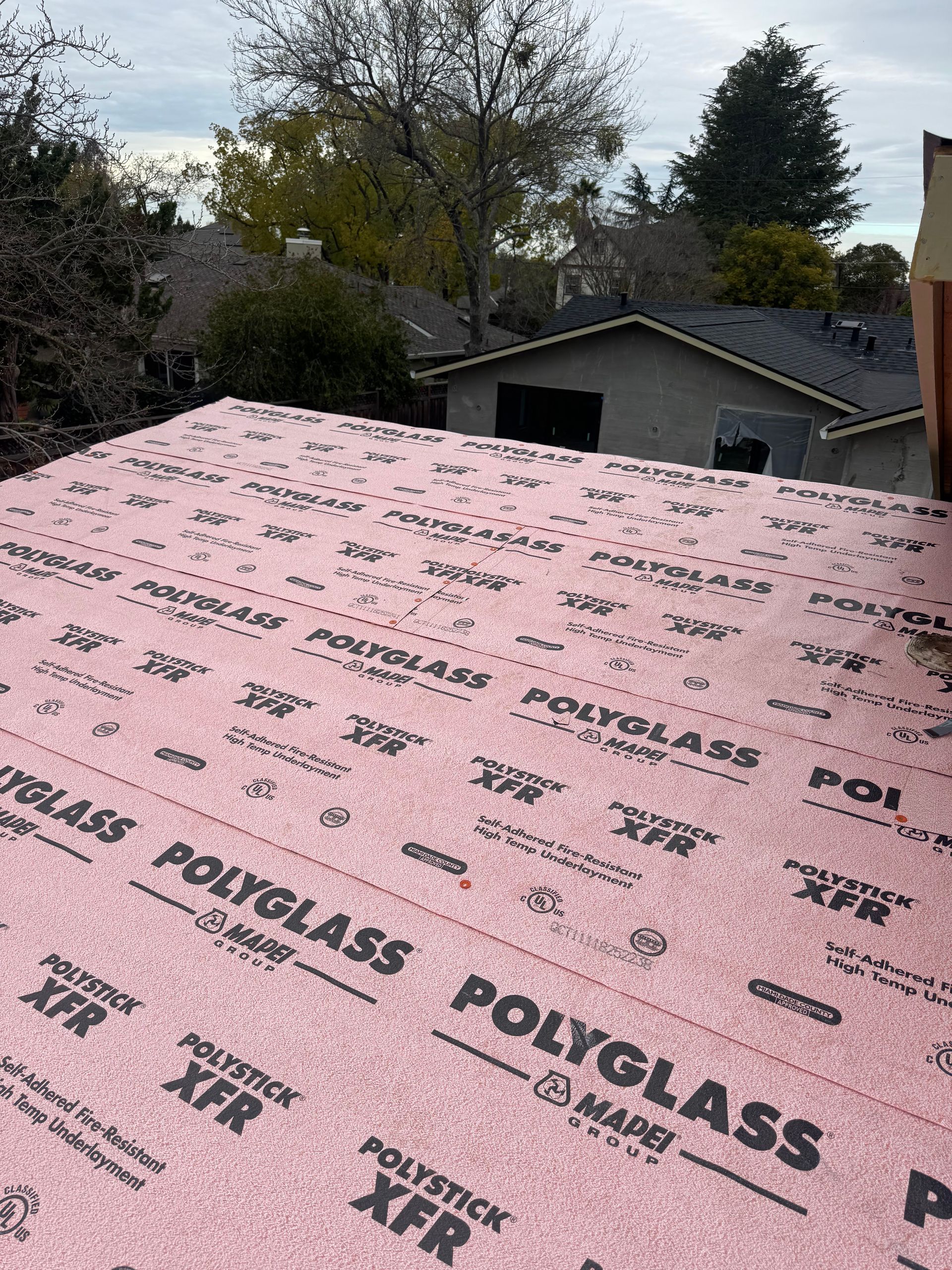 Pink roof underlayment on a house roof with trees and neighboring homes in the background