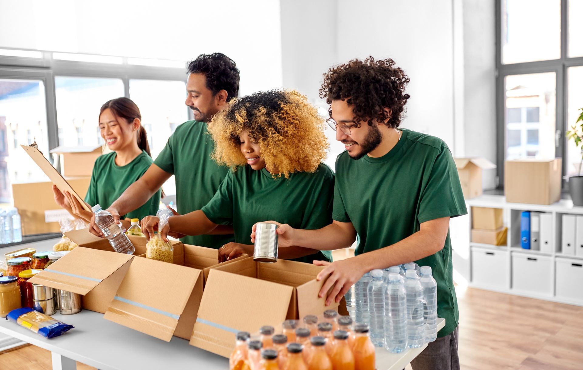 Volunteers in green shirts packing food into boxes in a bright room.