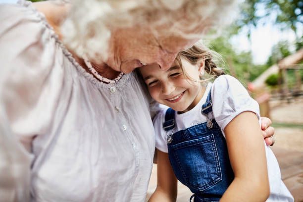 An elderly woman is hugging a little girl in a park.