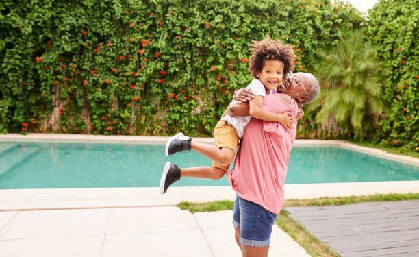 A man is holding a little boy in his arms in front of a swimming pool.