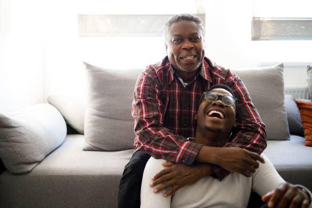 A man is sitting on a couch hugging another man.