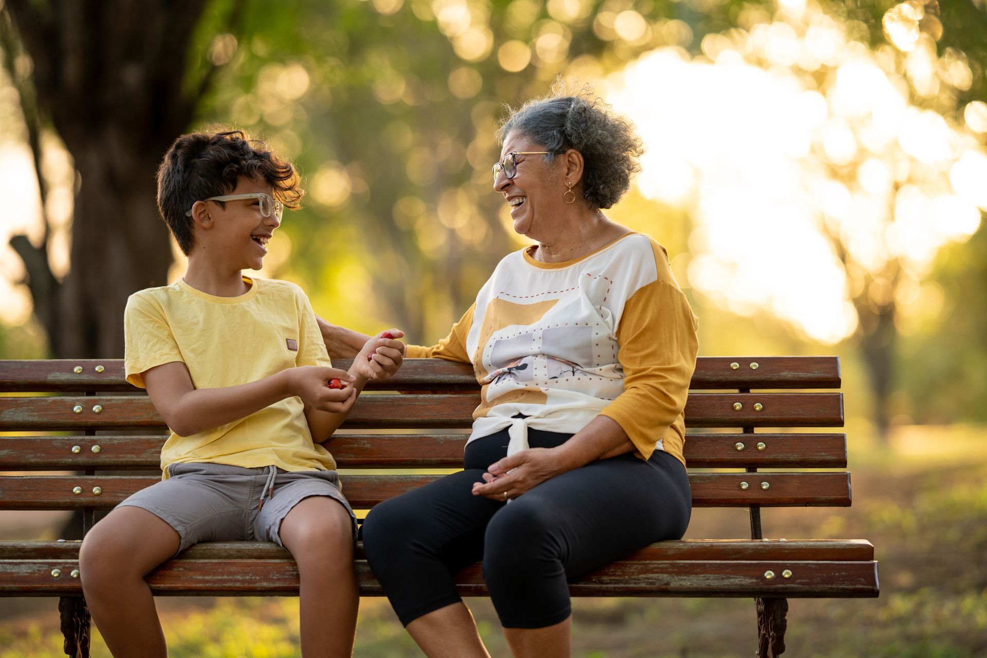 An elderly woman and a young boy are sitting on a park bench.