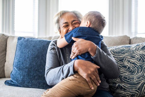 An elderly woman is sitting on a couch holding a baby.