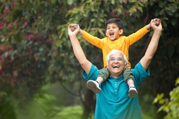 An elderly man is carrying a young boy on his shoulders.