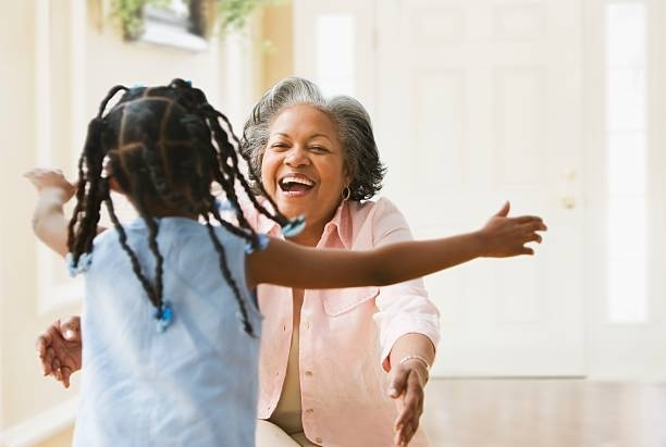 An elderly woman is hugging a young girl in a living room.