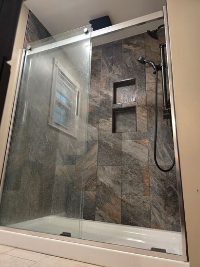 Shower with glass sliding door and stone tile interior; shower head on the right wall.