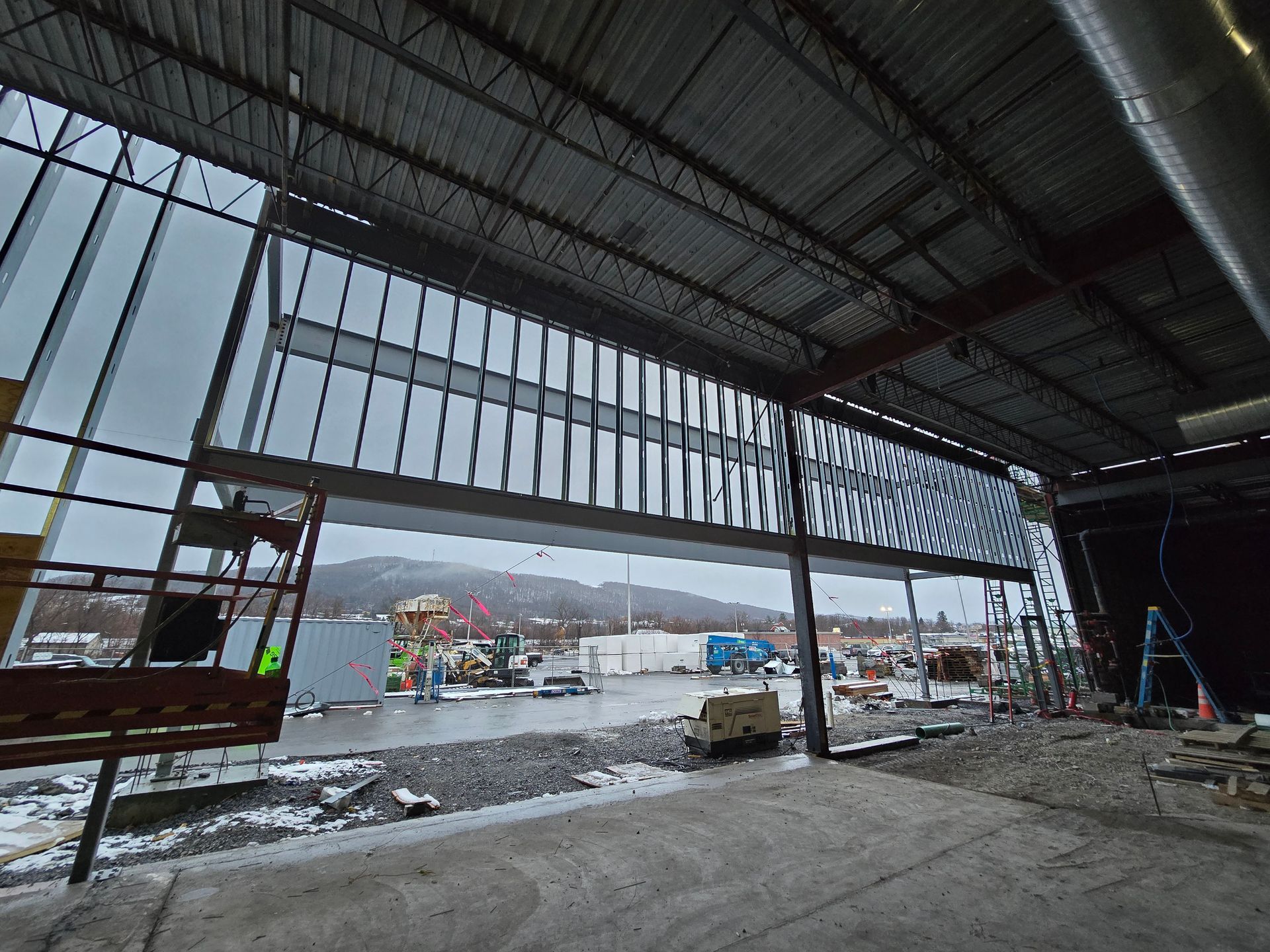 Interior view of a building under construction, looking out at a construction site and snow-covered ground.