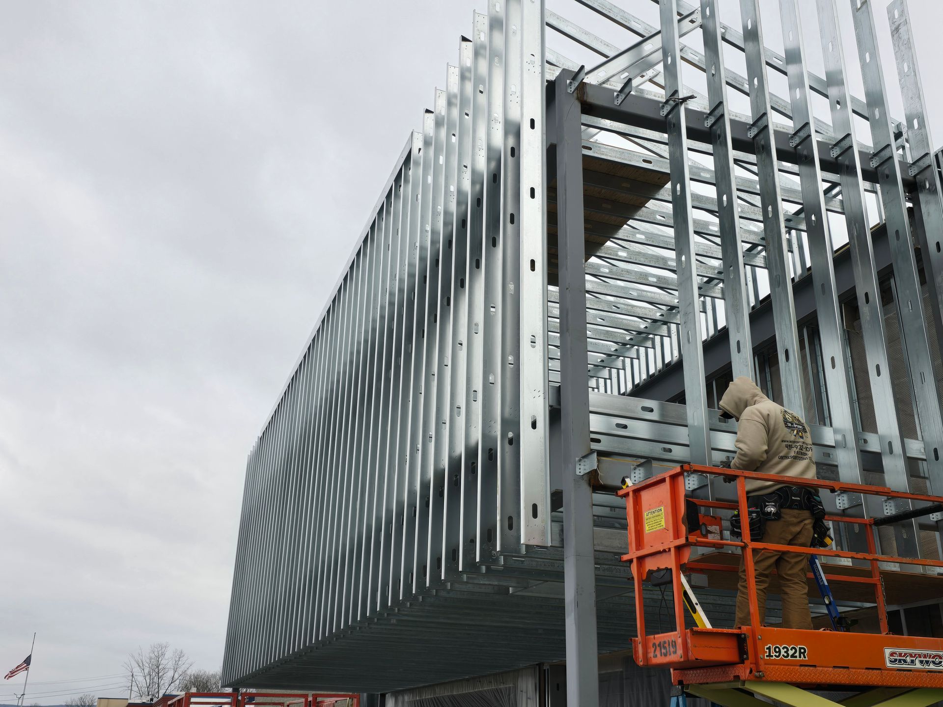 Construction worker on lift, installing metal facade on a building frame, cloudy sky overhead.