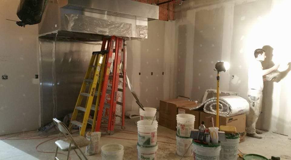 Construction of a kitchen with metal hood, ladders, drywall, buckets, and a person working.