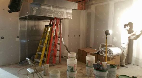 Construction of a kitchen with metal hood, ladders, drywall, buckets, and a person working.