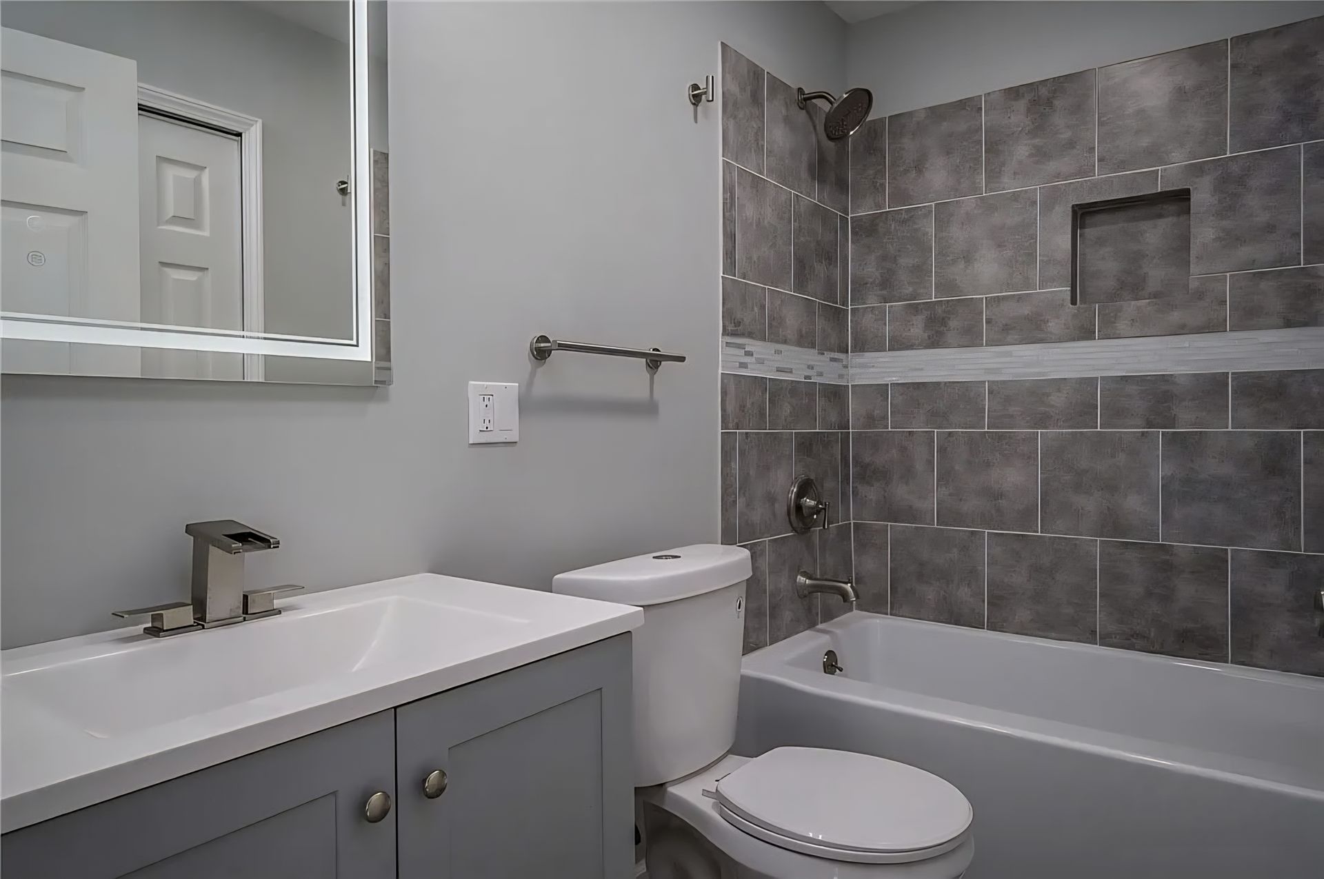 Bathroom with gray tiled shower and vanity, white toilet, and mirror.