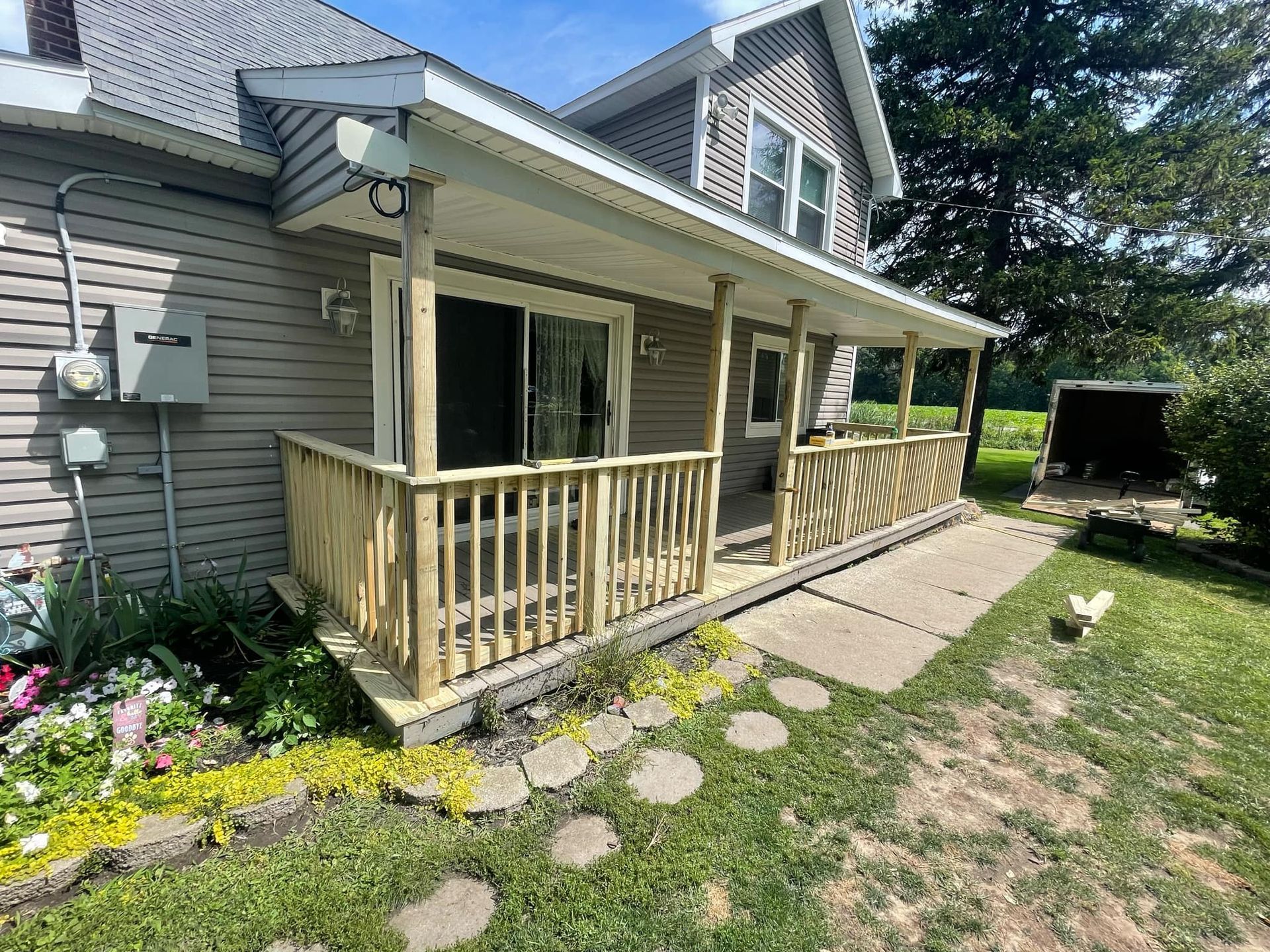 Wooden porch addition on a two-story gray house. A concrete walkway and lawn are in the foreground.