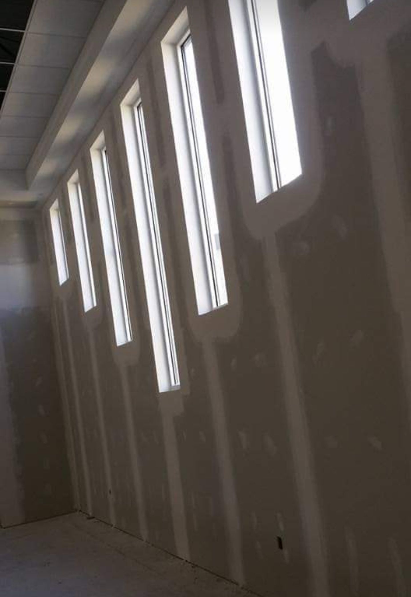 Row of tall, narrow windows in a room under construction, with drywall and bright sunlight.
